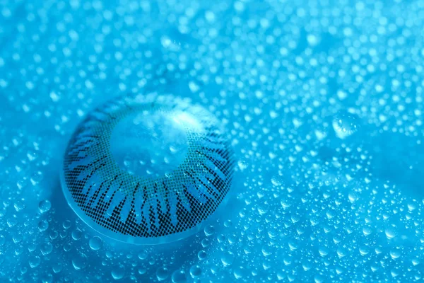 Contact lens and water drops on color background