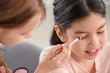 Sevimli küçük kız evde arkadaşının yüzüne makyaj yapıyor.