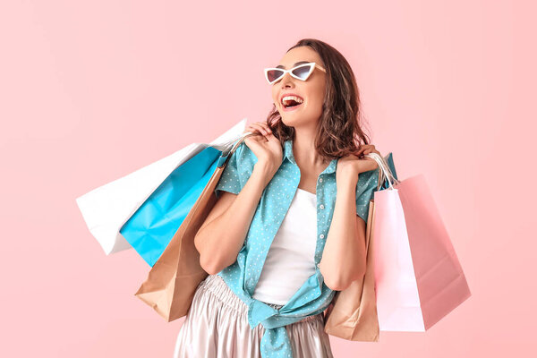 Beautiful young woman with shopping bags on color background