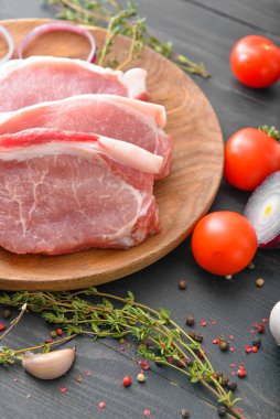 Koyu ahşap arka planda çiğ domuz eti, baharat ve sebze tabağı.