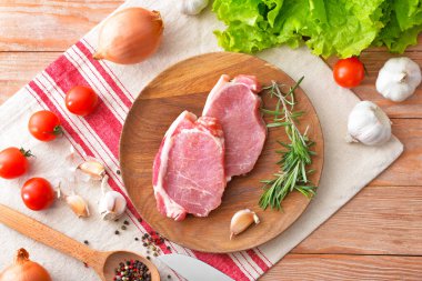 Ahşap zemin üzerinde çiğ domuz eti, sebze ve baharat tabağı.