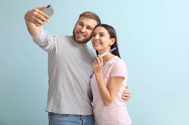 Hamilelik testi olan mutlu genç çift, arka planda selfie çekiyor.
