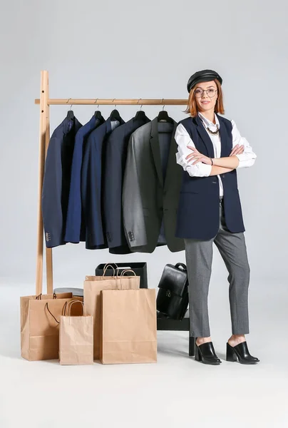 Female stylist near rack with male clothes on white background