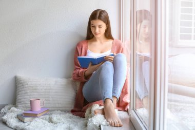 Evde kitap okuyan genç bir kadın.