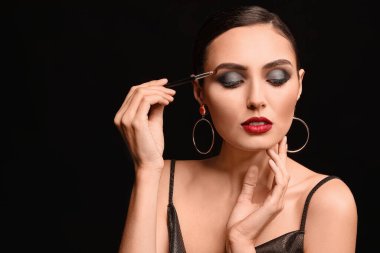 Beautiful young woman applying makeup against dark background