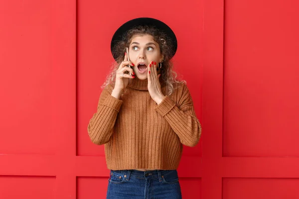 驚く若いです女性で暖かいセーターで電話で話す色の背景 — ストック写真