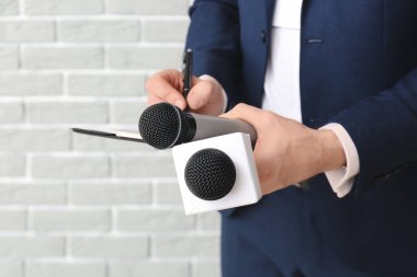 Tuğla arka planda mikrofonları olan erkek gazeteci, yakın plan