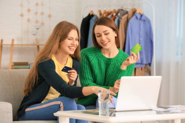 Evde online alışveriş için dizüstü bilgisayar kullanan genç kadınlar