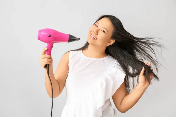 Beautiful Asian woman with hair dryer on light background