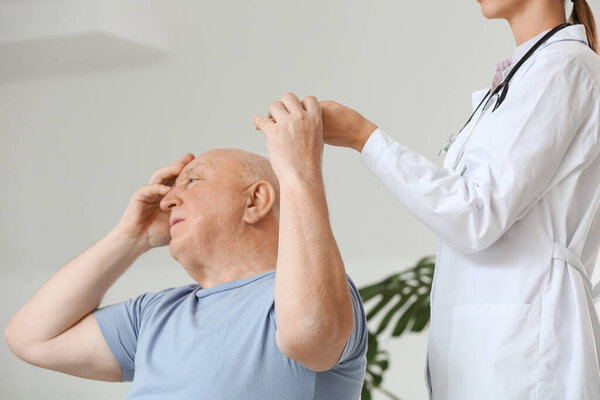 Female doctor working with senior man suffering from Parkinson syndrome in clinic