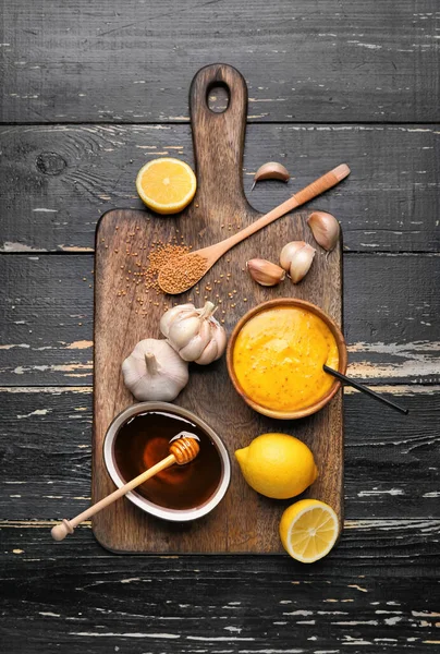 Bowl of tasty honey mustard sauce with ingredients on dark wooden background