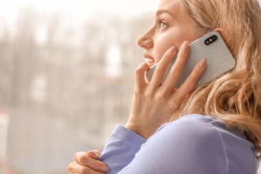 Evde cep telefonuyla konuşan genç bir kadın.