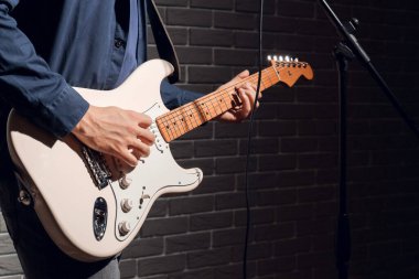 Koyu tuğla duvarın yanında gitar çalan genç bir adam.