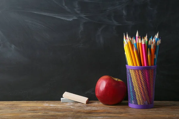 Apple, pencils and chalk on table in classroom