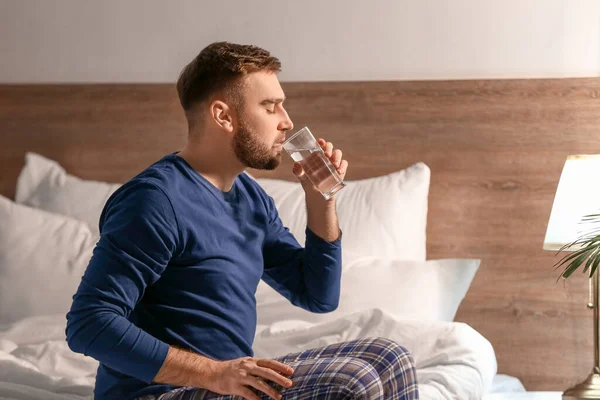Young man drinking water in bedroom at night