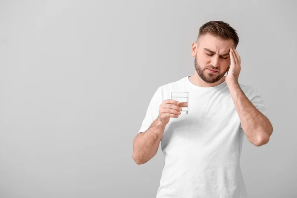 Jongeman Met Een Glas Water Met Hoofdpijn Een Lichte Achtergrond — Stockfoto