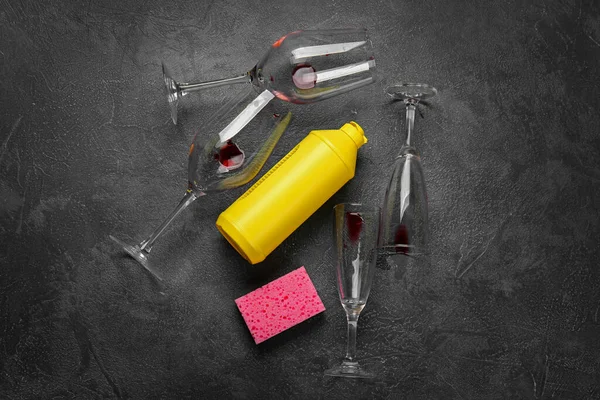 Dirty wineglasses and dish wash detergent on dark background