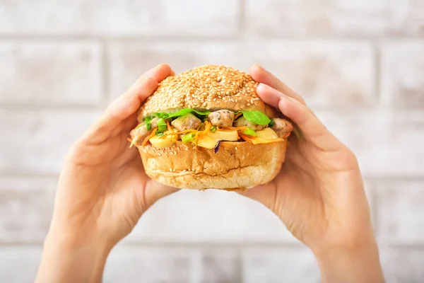 Female hands with tasty doner kebab in bun on brick background