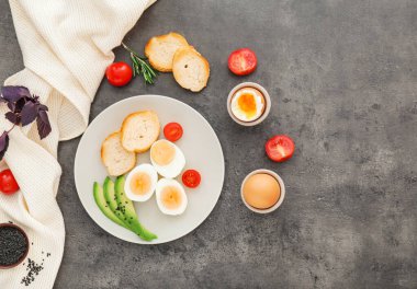 Haşlanmış yumurta, gri arka planda ekmek ve sebzeli tabak.