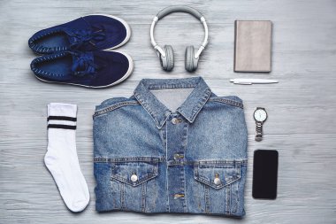 Ahşap arka planda aksesuarları, kulaklıkları ve cep telefonu olan şık erkek kıyafetleri.