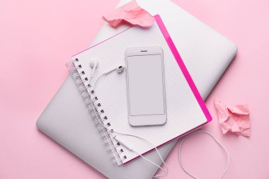 Pembe arka planda dizüstü bilgisayarı ve defteri olan cep telefonu.