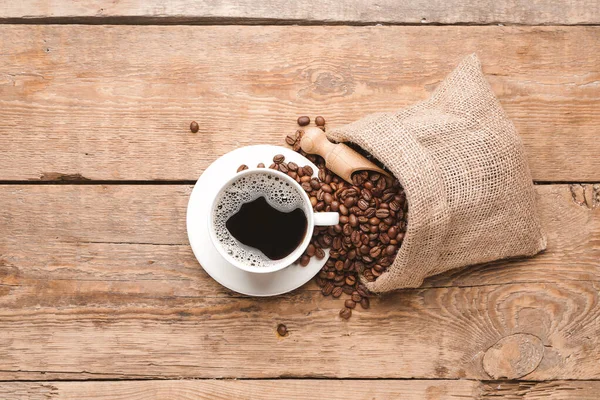 Beutel Mit Kaffeebohnen Und Tasse Heißgetränk Auf Holzgrund — Stockfoto