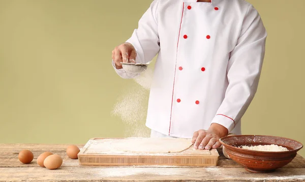 Man sieving flour over dough on table