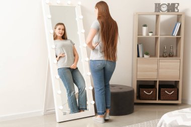 Güzel genç bir kadın aynadaki yansımasına bakıyor.