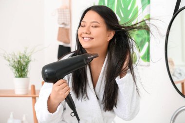 Evde saç kurutma makinesi olan güzel bir Asyalı kadın.