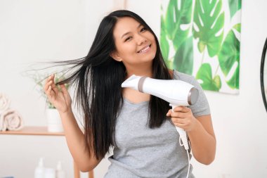 Evde saç kurutma makinesi olan güzel bir Asyalı kadın.