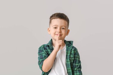 Gri arka planda sessizlik jesti yapan sevimli küçük çocuk.