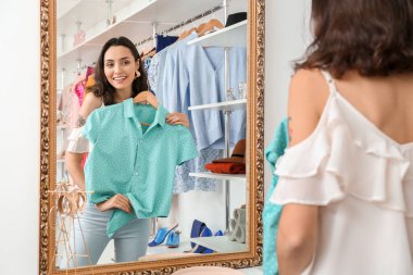 Mağazada aynanın yanında yeni giysileri olan güzel genç bir kadın.