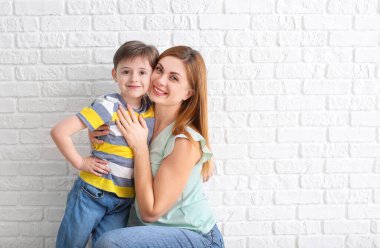 Mutlu küçük çocuk ve annesi beyaz tuğla duvarın yanında