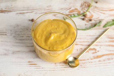 Glass of tasty honey mustard sauce on white wooden table