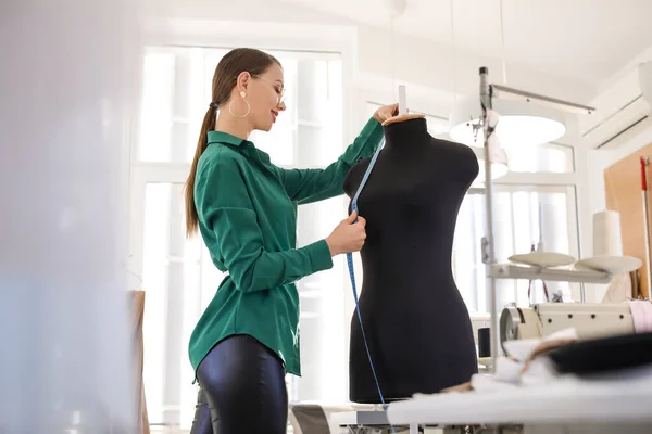 Portrait of female tailor near mannequin in workshop
