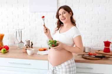 Güzel hamile kadın mutfakta sağlıklı salata yeme