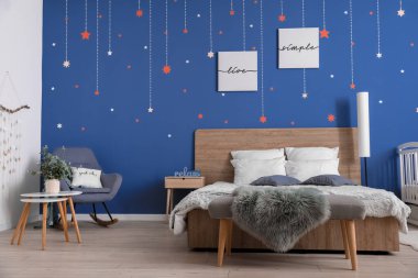 Mavi duvarın yanında büyük yatağı olan şık bir oda.