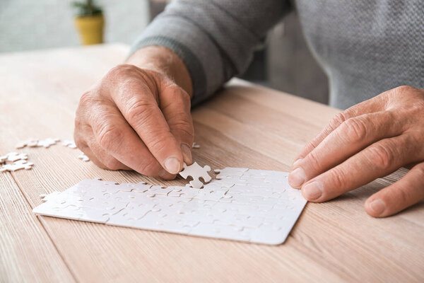 Senior man with Parkinson syndrome doing puzzle at home, closeup