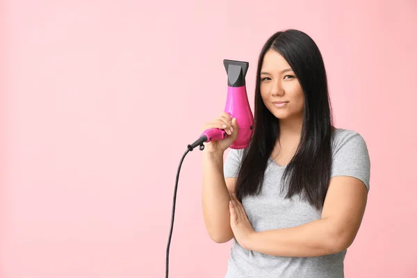 Beautiful Asian woman with hair dryer on color background