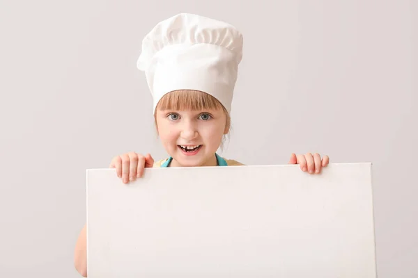 Cute little chef with blank poster on light background