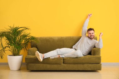 Genç adam evdeki kanepede otururken müzik dinliyor.