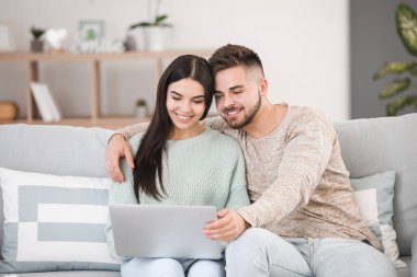 Evde kanepede otururken dizüstü bilgisayar ile genç çift