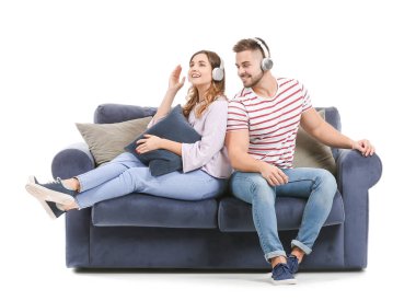 Genç çift, beyaz arka planda kanepede otururken müzik dinliyor.