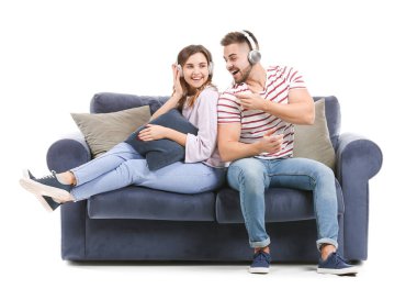Genç çift, beyaz arka planda kanepede otururken müzik dinliyor.