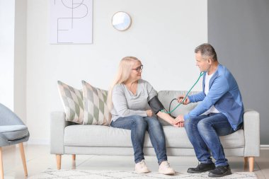 Olgun bir adam evinde karısının kan basıncını ölçüyor.