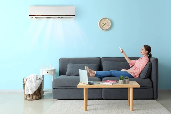 Young woman switching on air conditioner at home