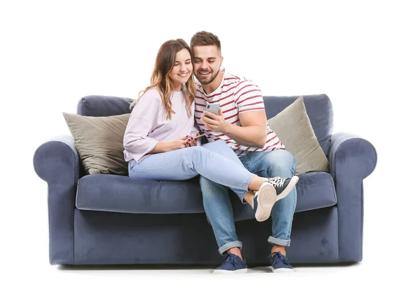 Young couple with mobile phones sitting on sofa against white background