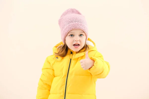 かわいいです女の子で冬服ショー親指アップジェスチャー上の光の背景 — ストック写真