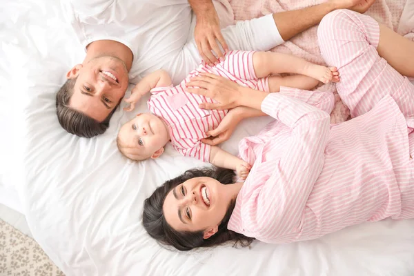Cute baby with parents lying on bed, top view