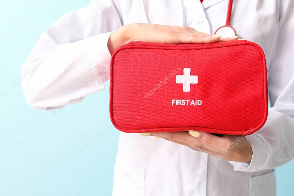 Female paramedic with first aid kit on color background, closeup